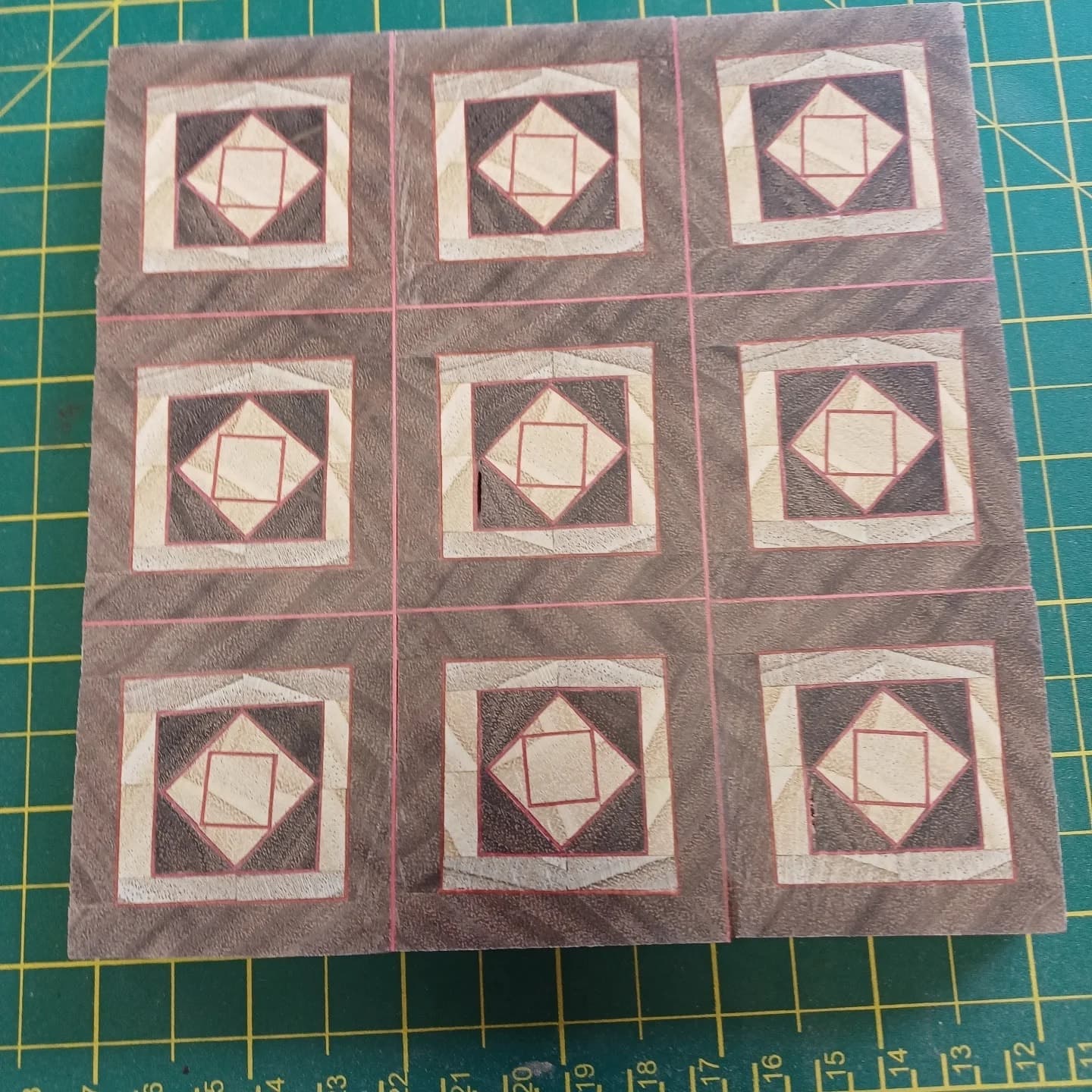 A finished box lid on a cutting mat, nine squares of concentric diamonds cut from red, cream and dark woods.
