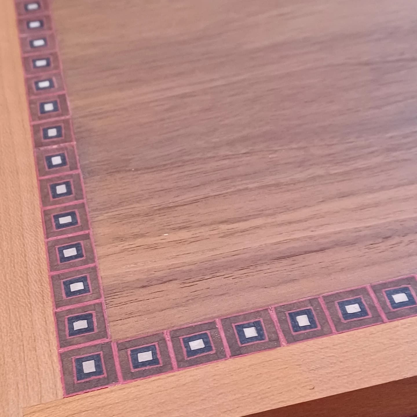 A close view of an inlaid border, small pink, navy and white squares set into walnut.