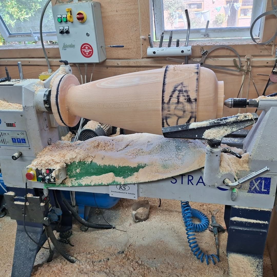 A pale beech blank mounted on the lathe, with shavings from the last one still on the floor
