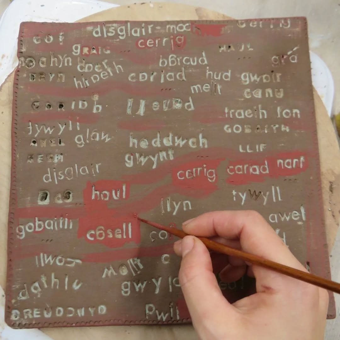 A hand painting Welsh words onto a clay slab in red and white slip