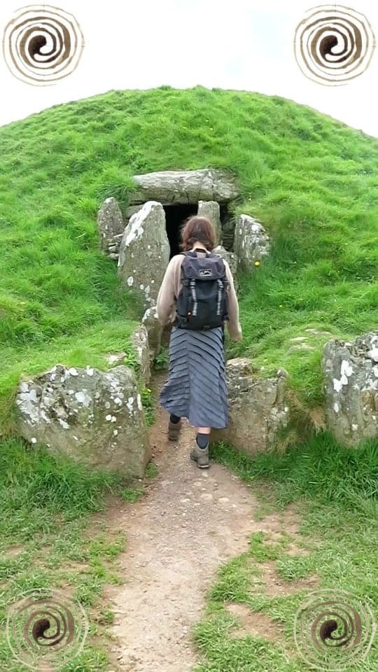 Bethan walking into the entrance passage of a grass-covered Neolithic chambered tomb