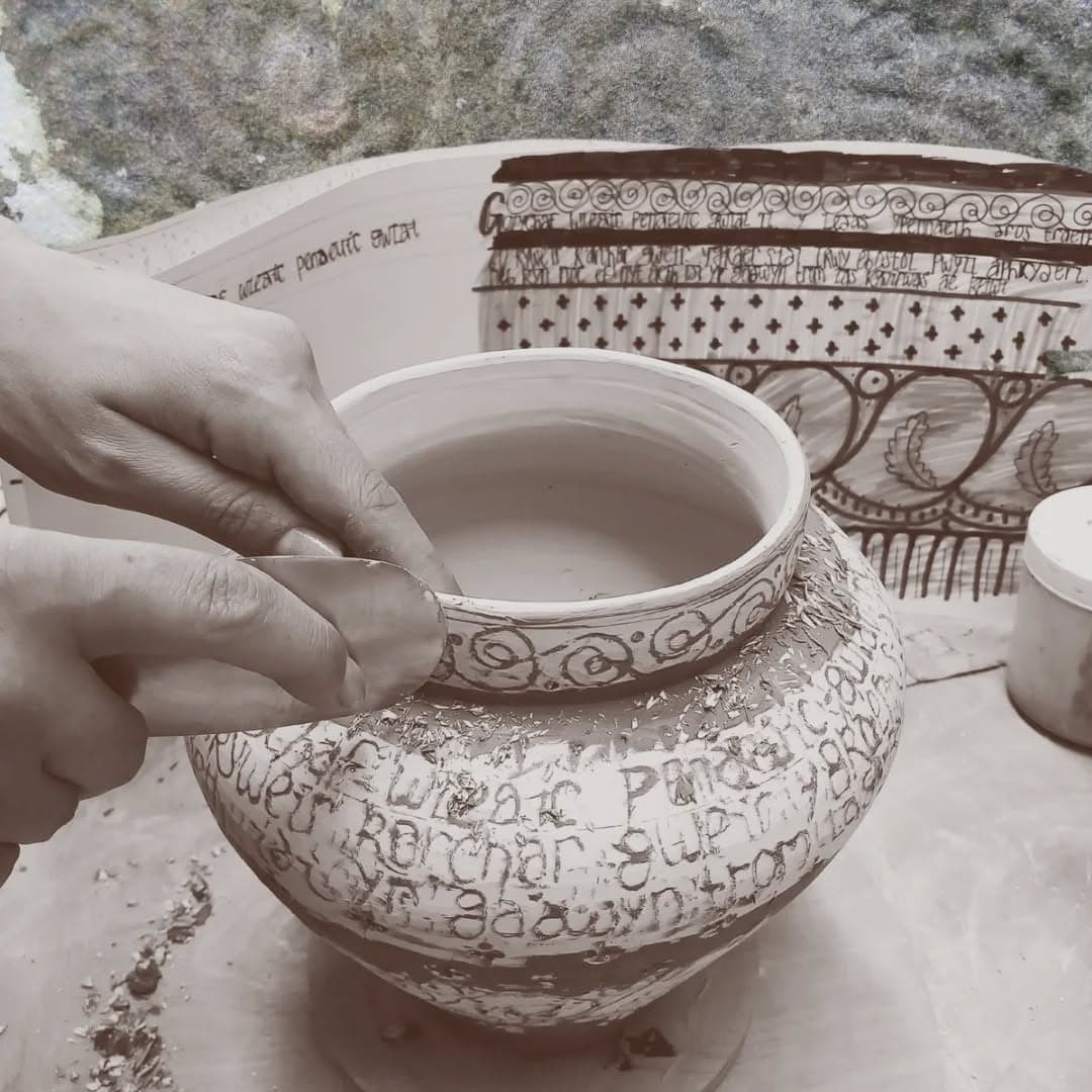 Hands scraping back slip decoration on a large ceramic vessel covered in Welsh text