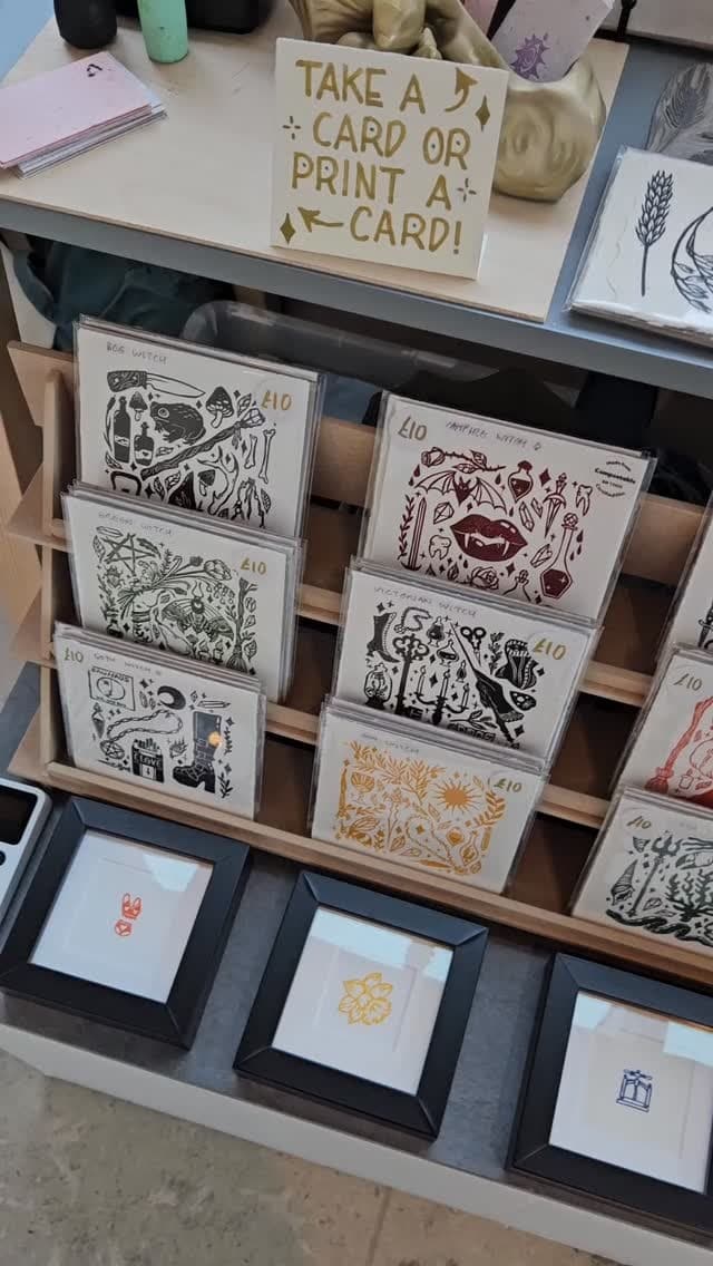Her market stall, prints in the racks and a sign inviting you to print your own card.