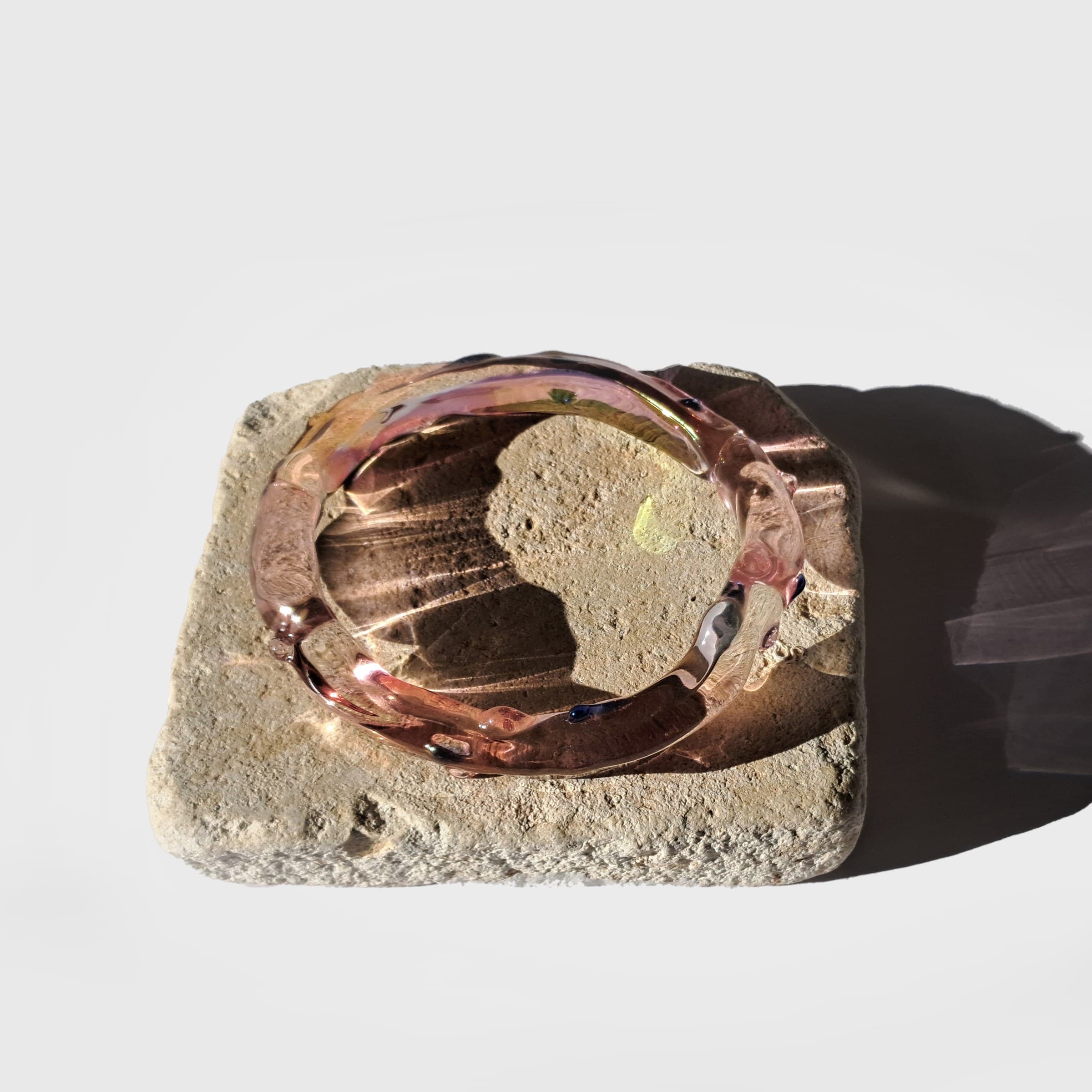 A pink glass bangle resting on a piece of stone, casting a long shadow