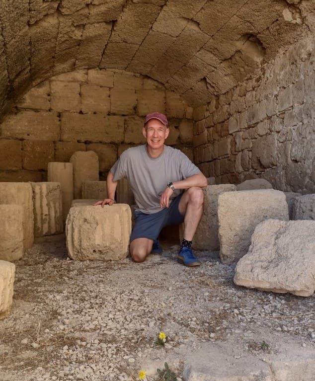 Greig Alderman sitting among ancient stone ruins in Greece