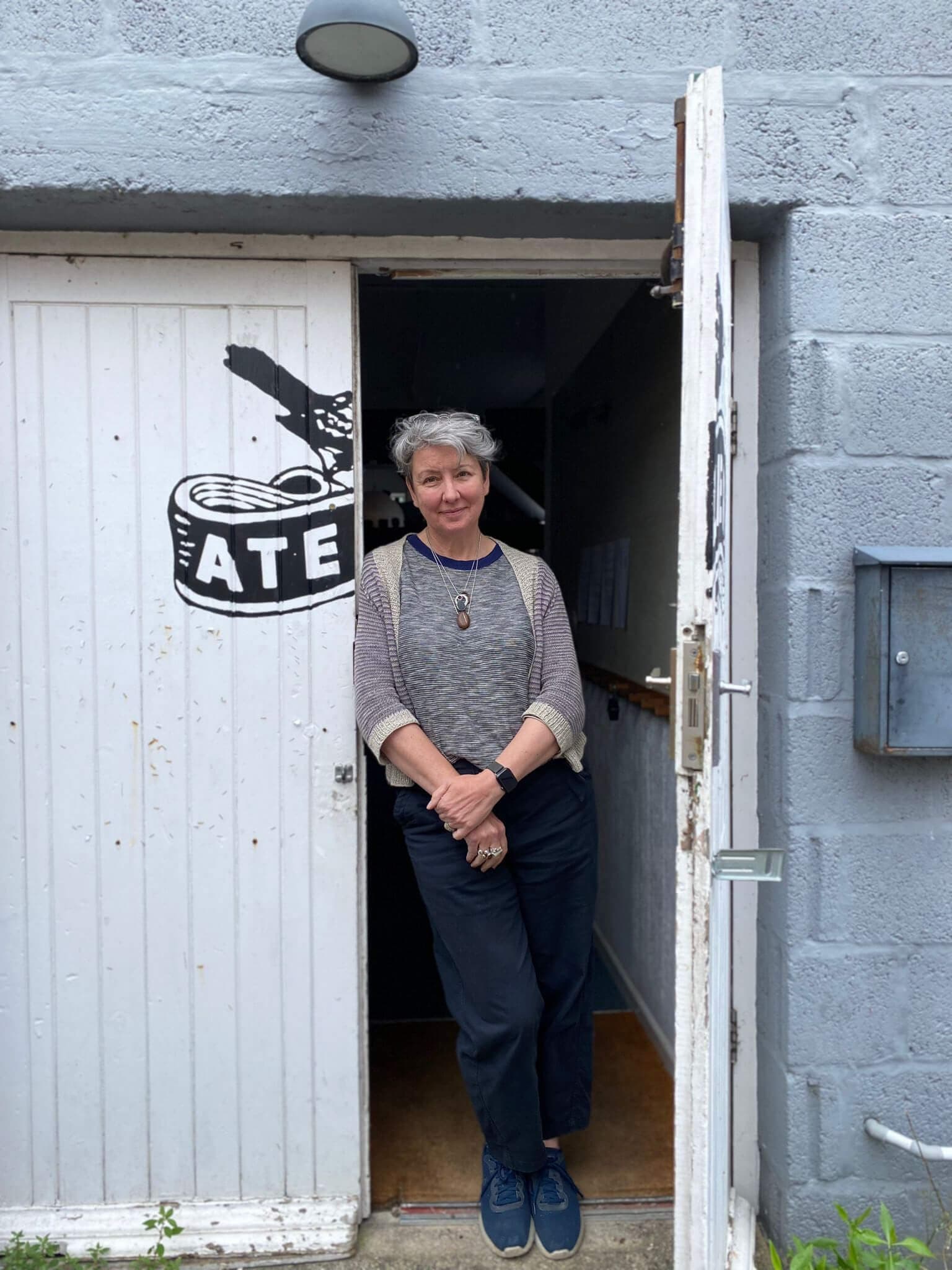 Woman with grey hair standing in doorway of stone building with white-painted wooden door