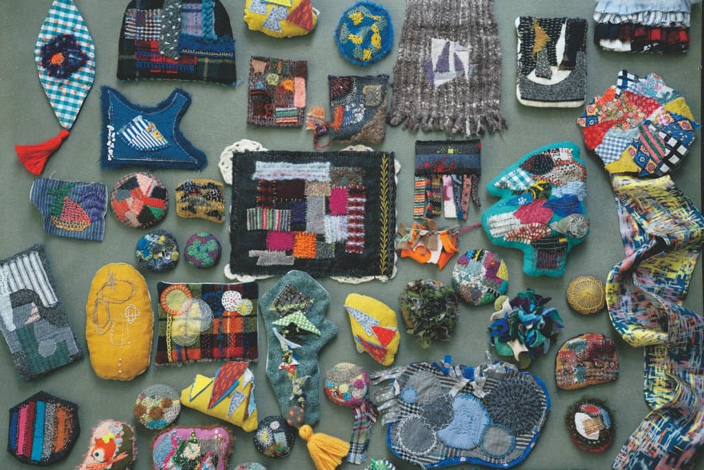 Colourful collection of darned and mended textile pieces arranged on grey background, including patched fabrics