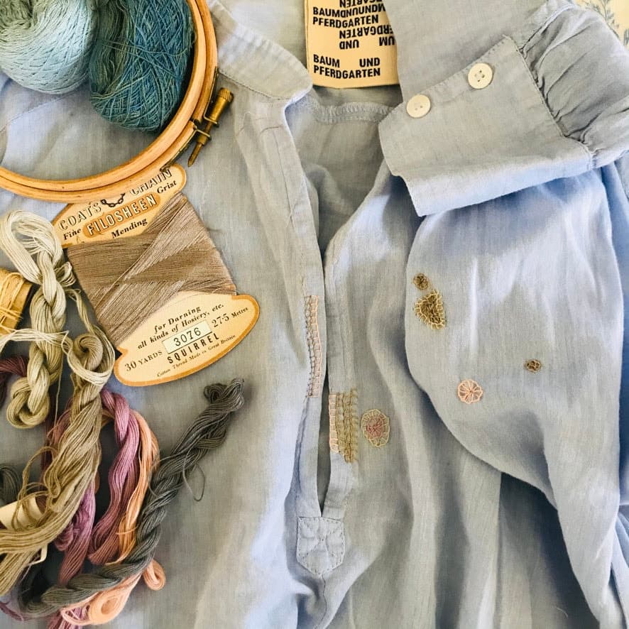 Flat lay of embroidery and mending supplies: wooden hoop with teal thread, wooden labels