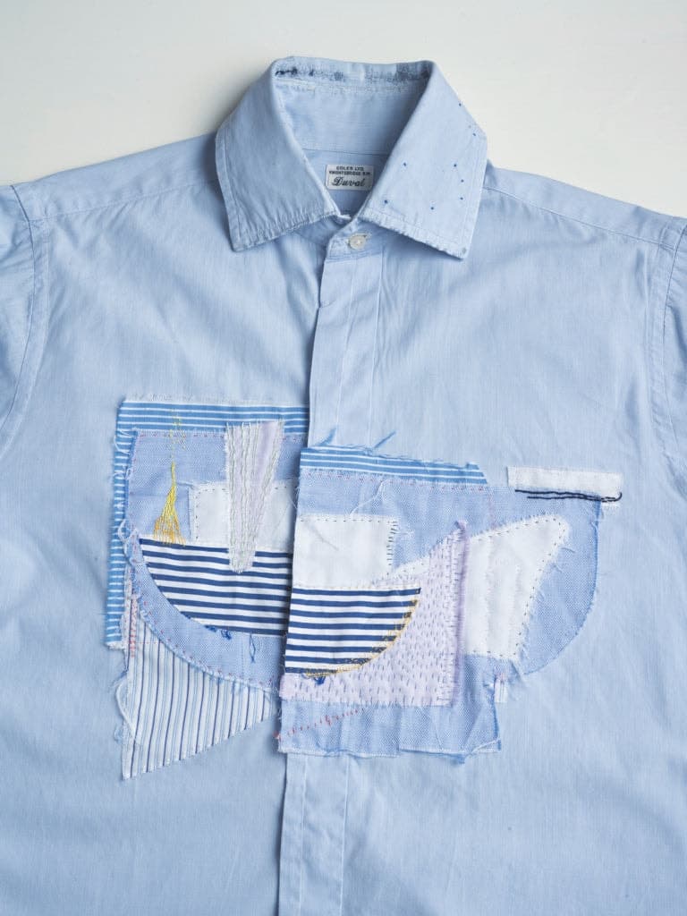 Light blue shirt with two patch pockets featuring appliquéd and stitched textile fragments in blue