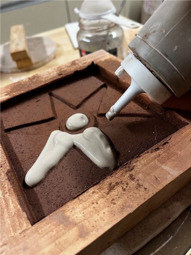Bottle piping white clay slip into a star-shaped hollow in red clay held in a wooden tile mould