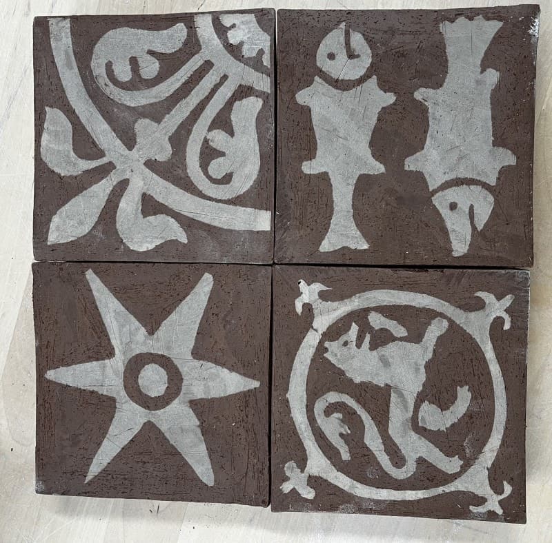 Four unfired inlaid tiles drying: a foliage design, two pike, a six-pointed star and a lion in a circle
