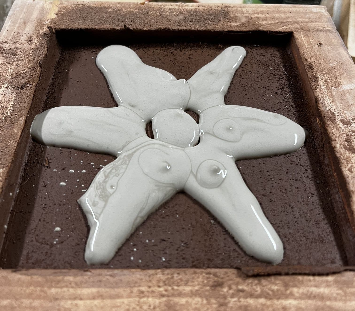 Six-pointed star of glossy white clay filling the stamped hollow of a red clay tile in a wooden mould