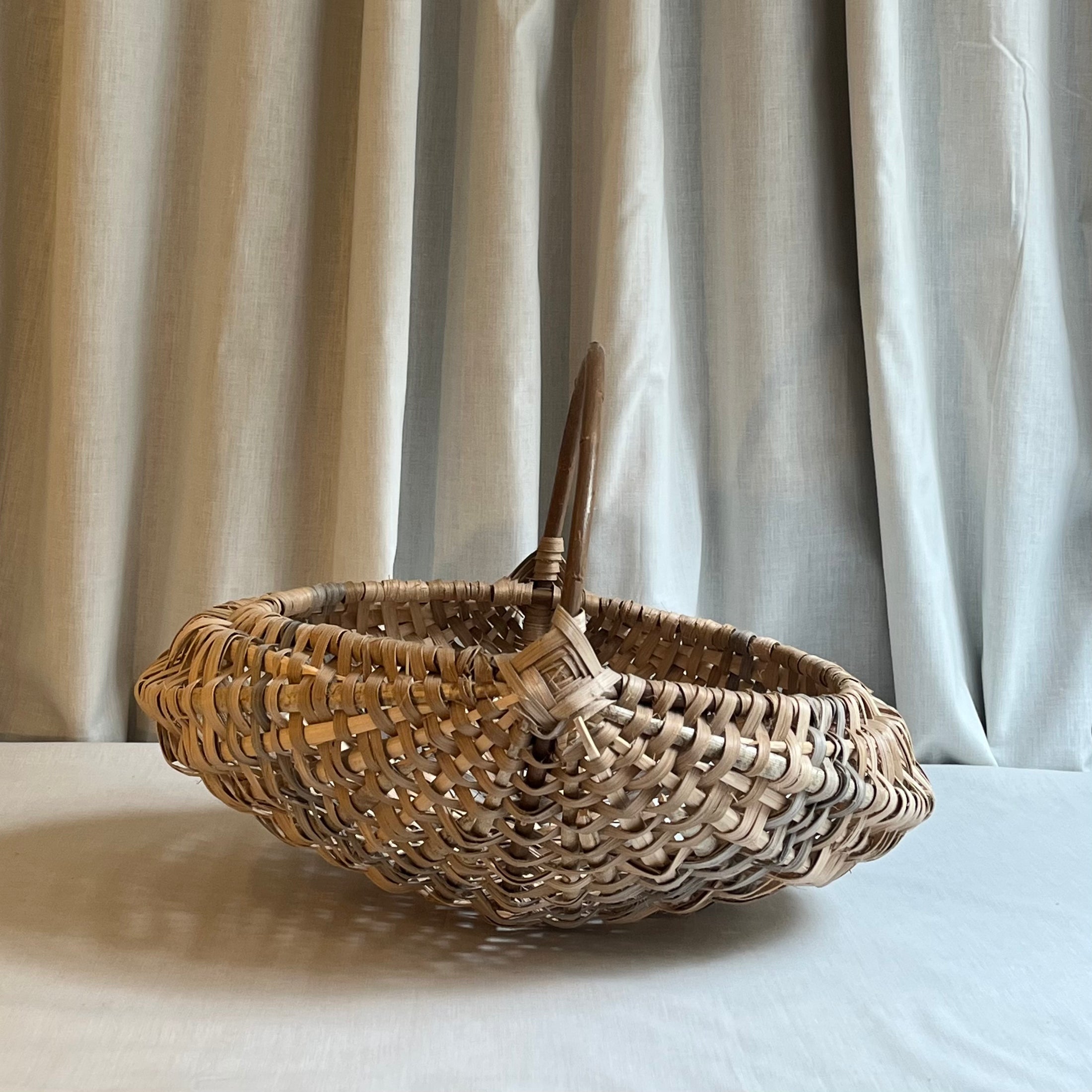 Woven basket with a handle on a light surface with a neutral curtain background