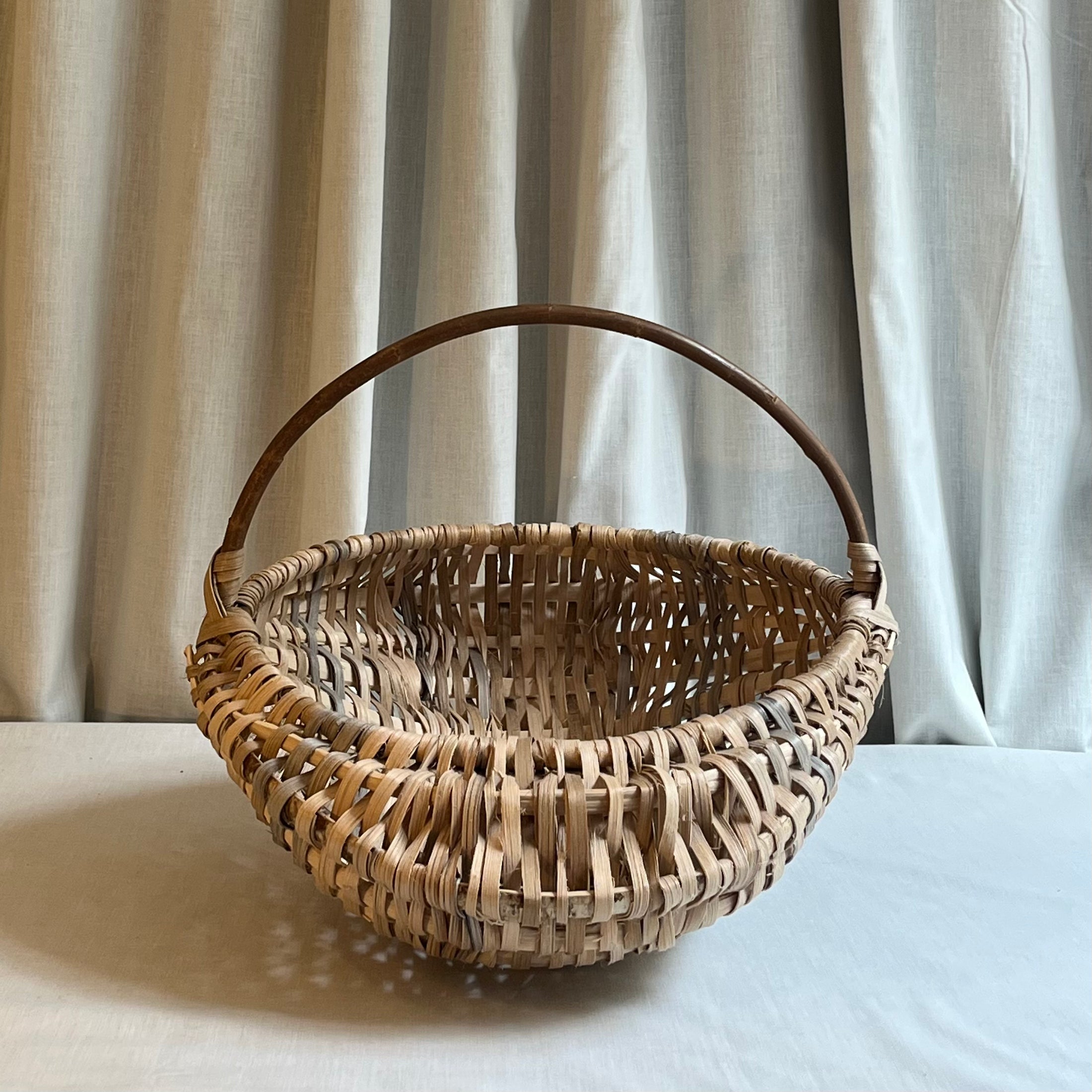 Woven basket with a handle on a light surface with curtains in the background