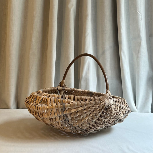 Woven basket with a handle on a light surface with a neutral curtain background