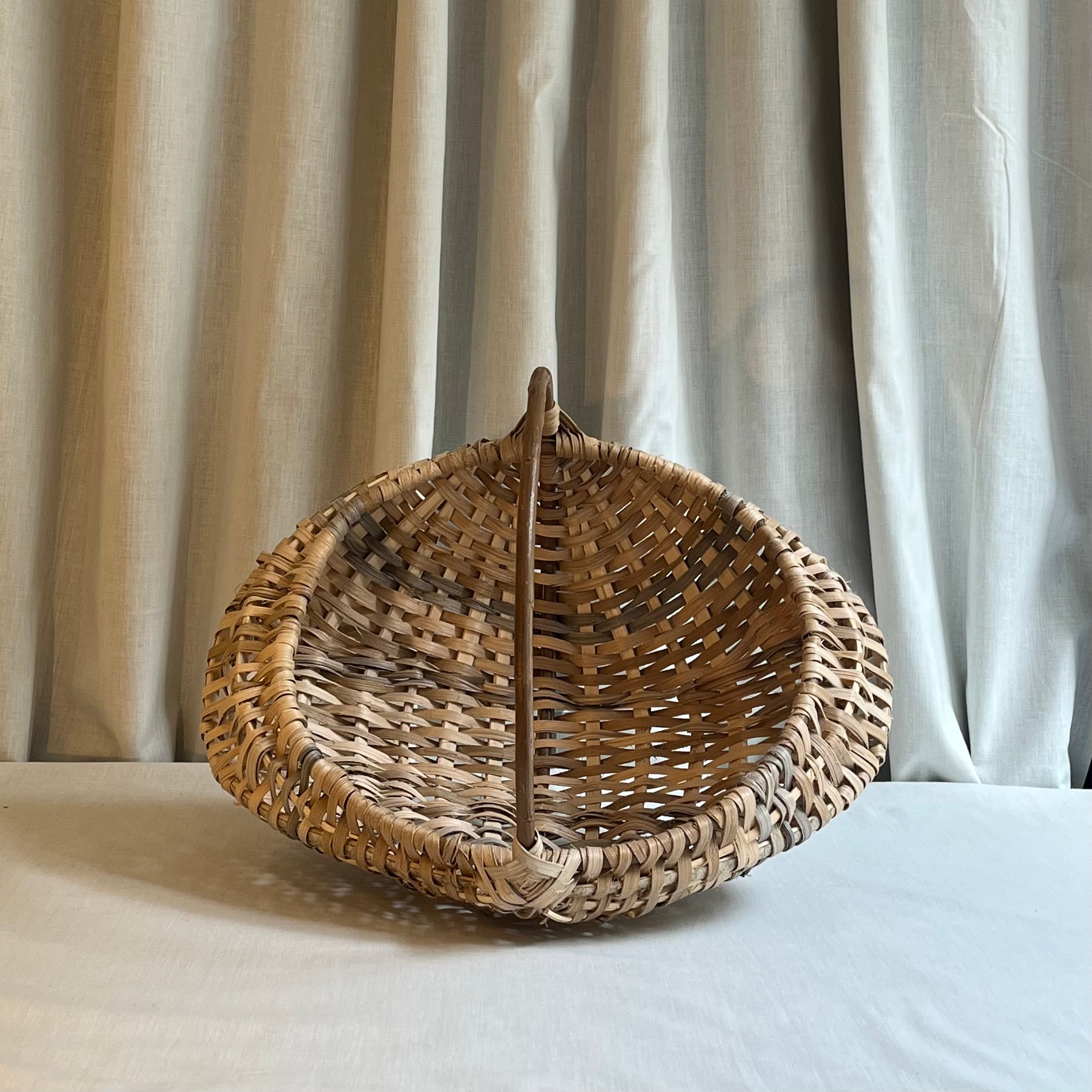 Woven basket with a handle on a light surface with curtains in the background