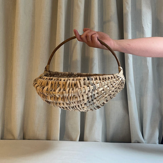 Hand holding a woven basket against a neutral curtain background