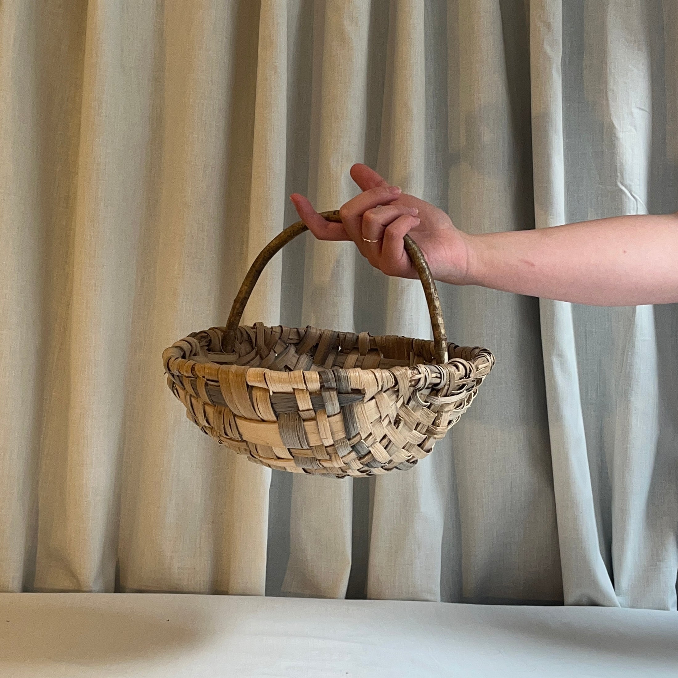 Hand holding a woven basket against a neutral curtain background