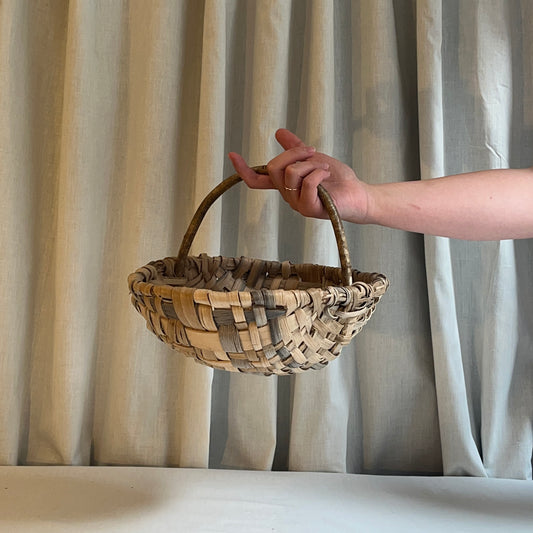 Hand holding a woven basket against a neutral curtain background
