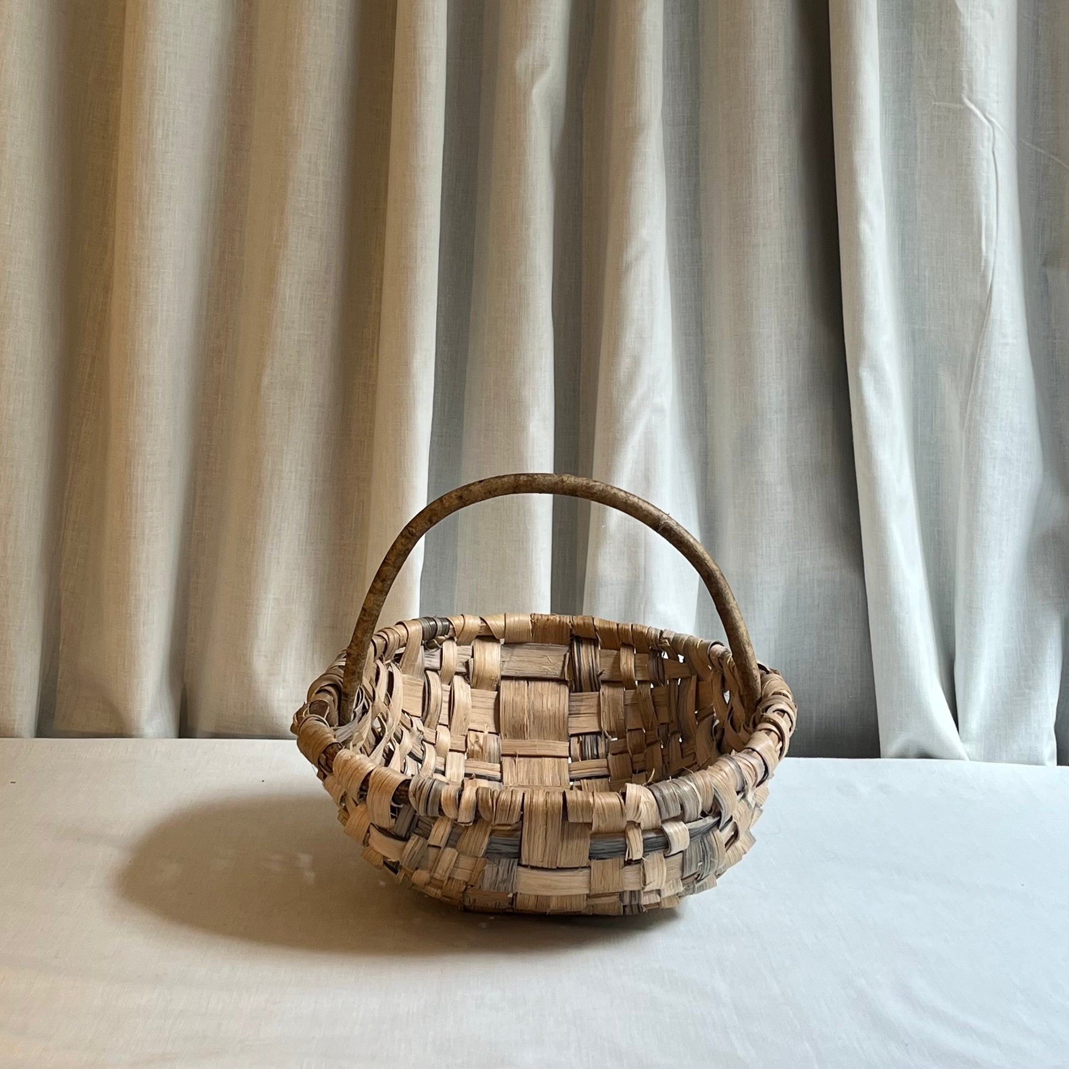 Woven basket with a handle on a light surface with a neutral curtain background
