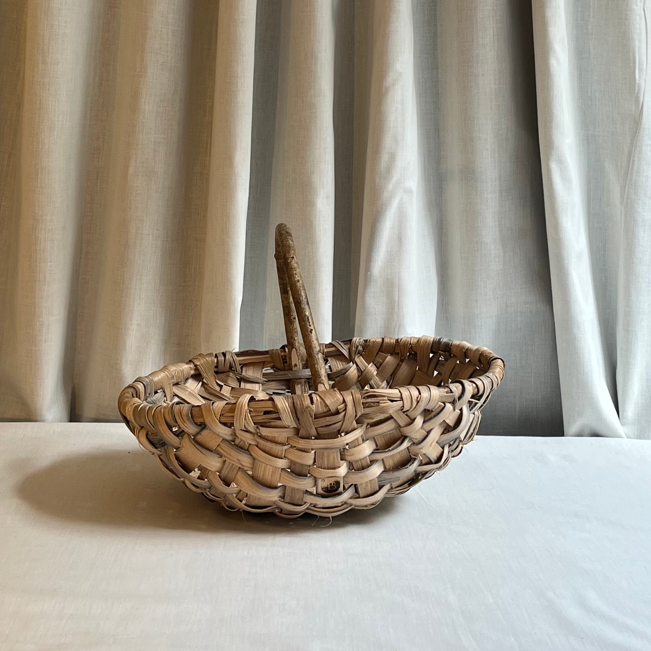 Woven basket with a handle on a white surface with a neutral curtain background