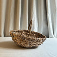 Load image into Gallery viewer, Woven basket with a handle on a white surface with a neutral curtain background
