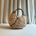 Load image into Gallery viewer, Woven handbag on a light surface with curtains in the background
