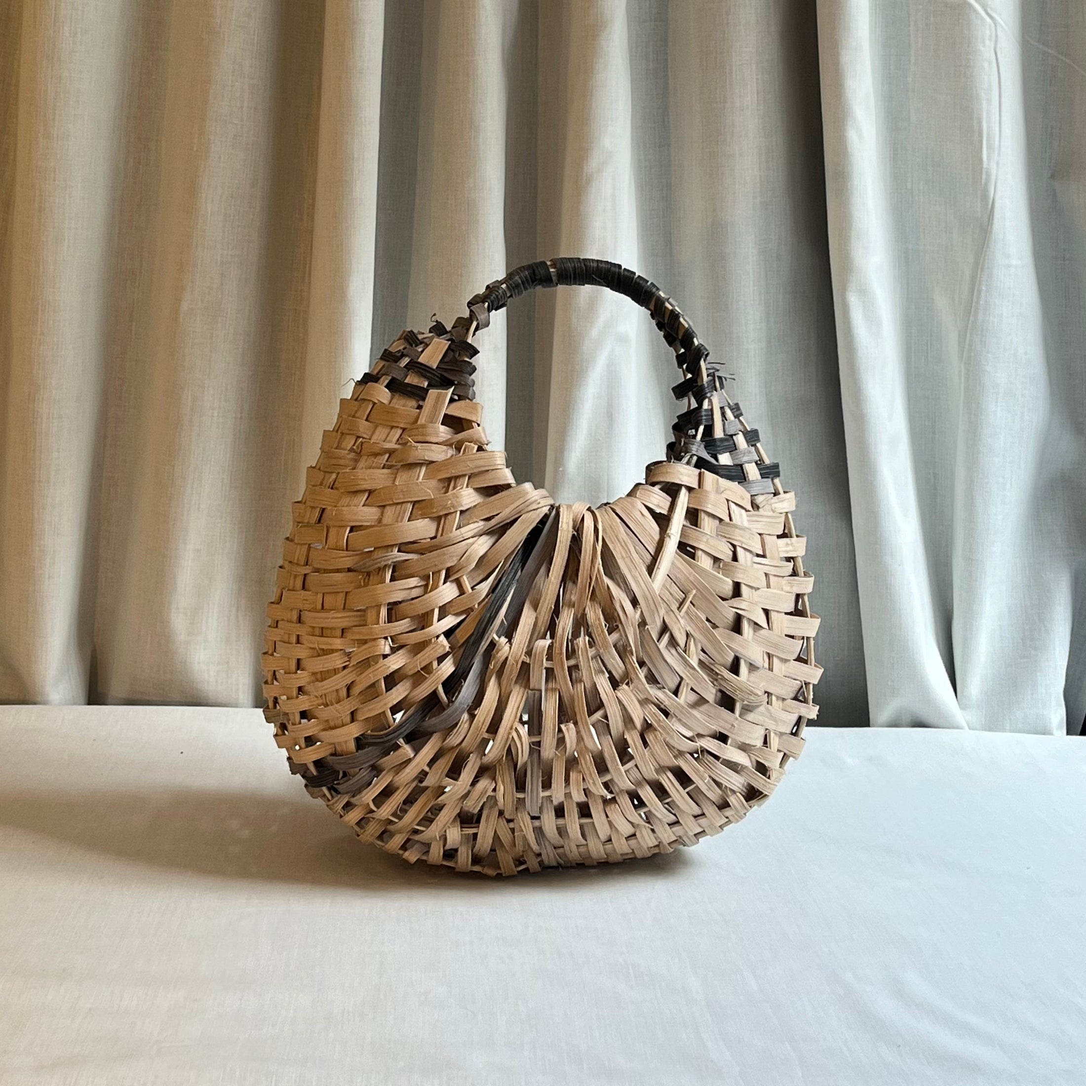 Woven handbag on a light surface with curtains in the background