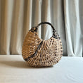 Load image into Gallery viewer, Woven handbag on a light surface with curtains in the background
