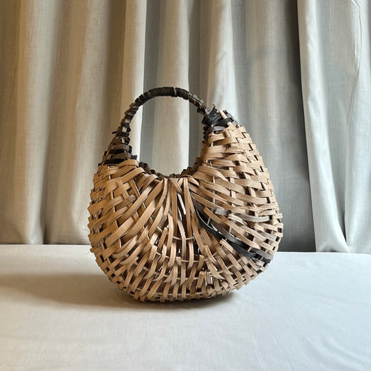 Woven handbag on a light surface with curtains in the background
