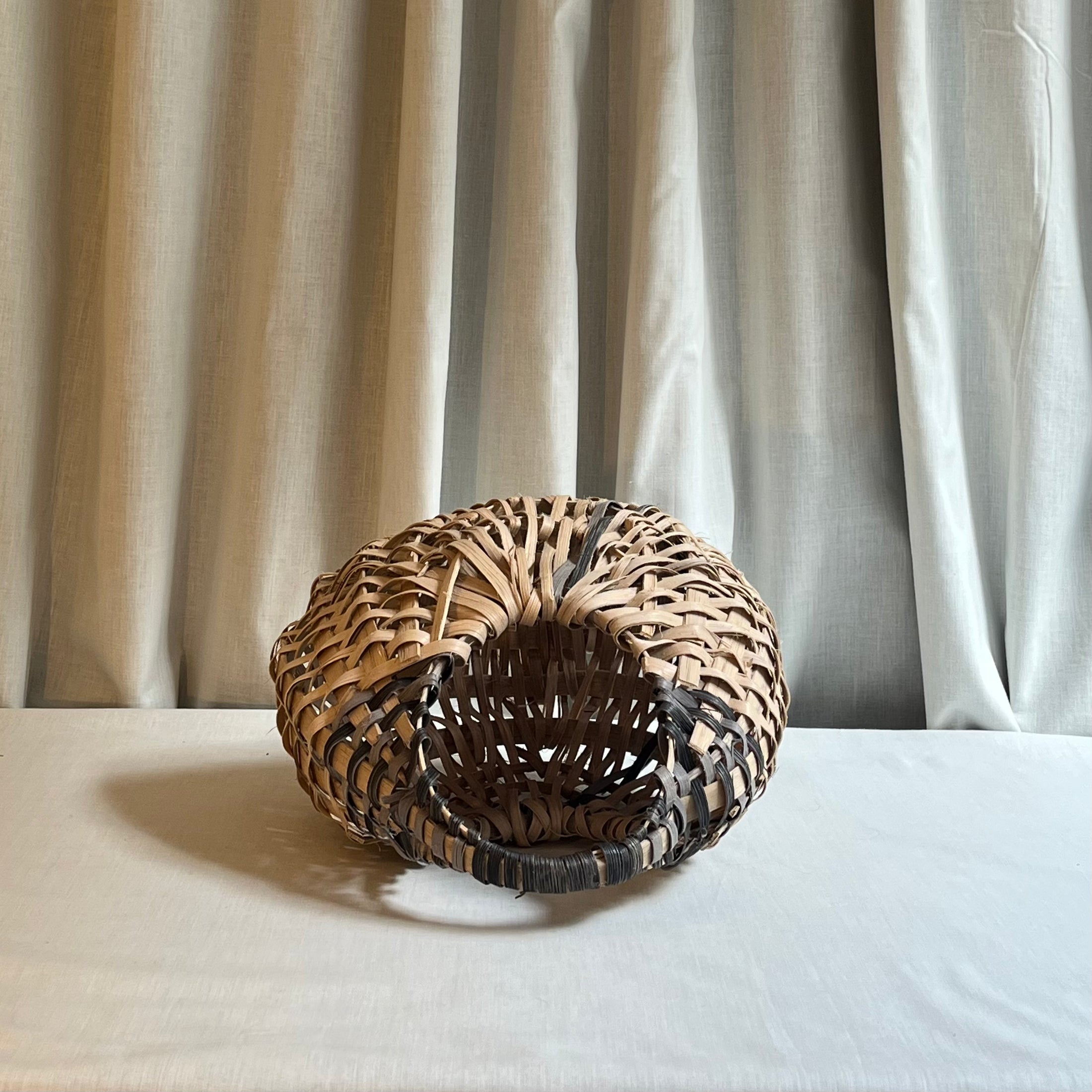 Woven basket on a white surface with a neutral curtain background