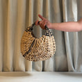 Load image into Gallery viewer, Hand holding a woven handbag against a neutral curtain background
