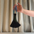 Load image into Gallery viewer, Hand holding a black brush with blue handle against a striped curtain background
