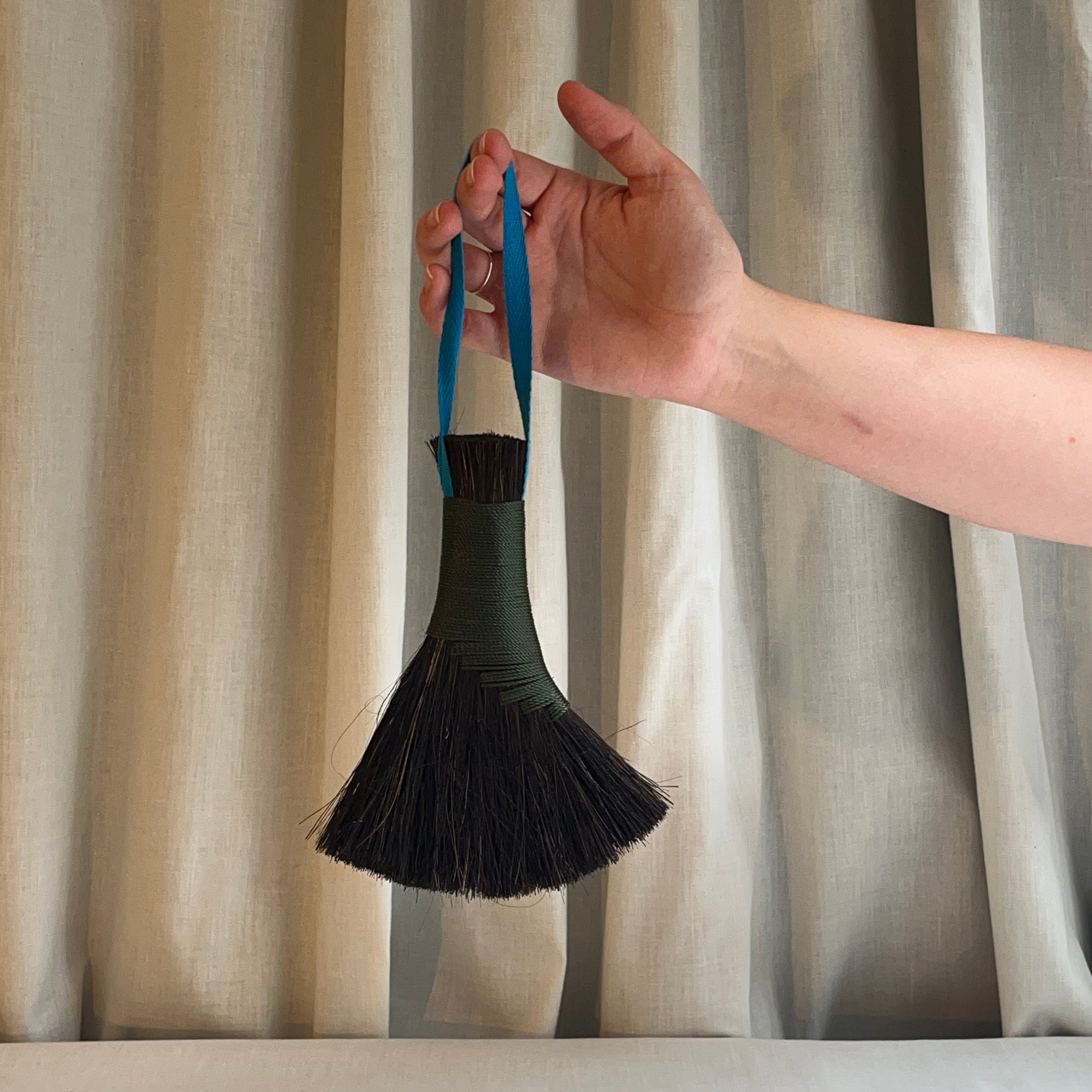 Hand holding a black brush with blue handle against a striped curtain background