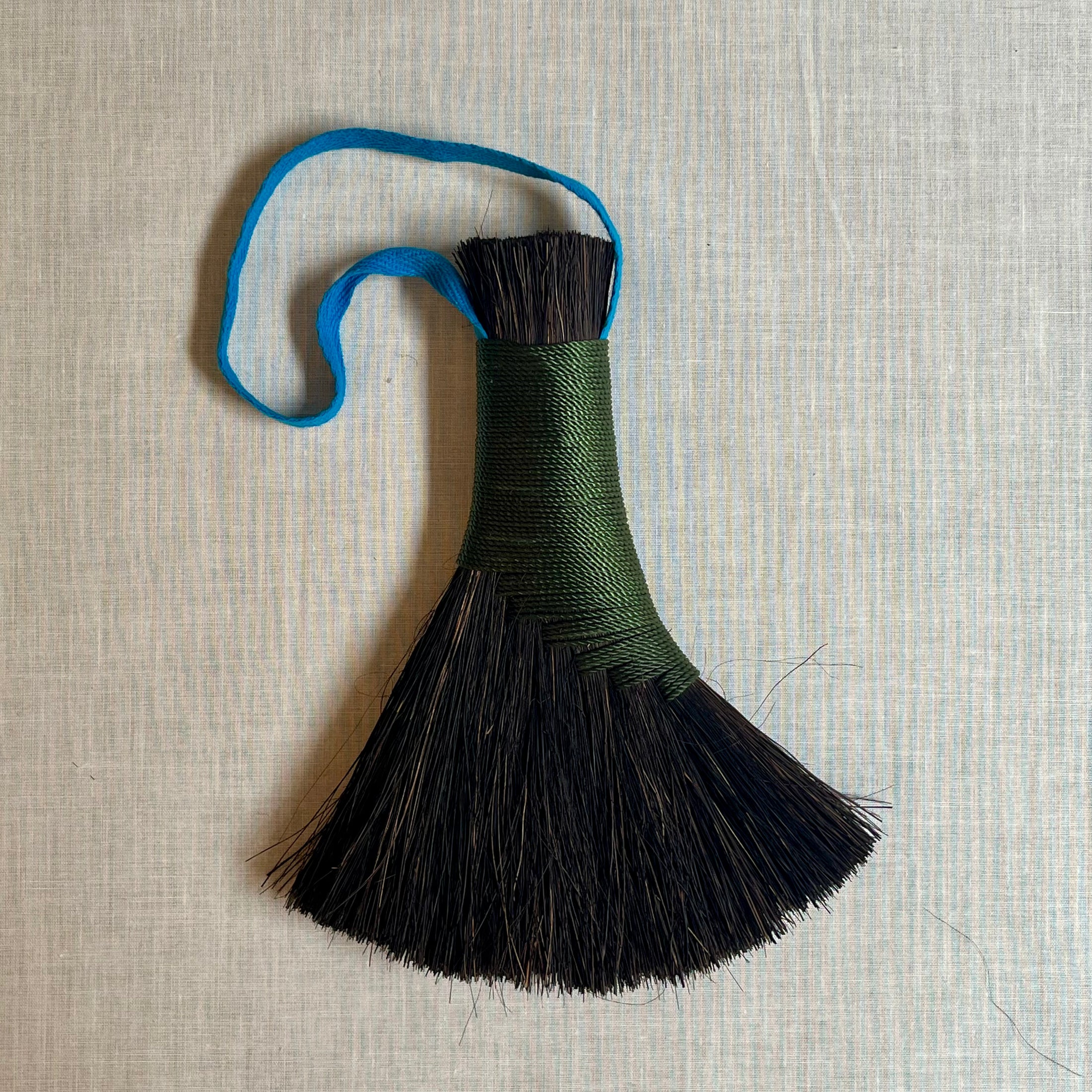 Decorative broom with black bristles and a colorful handle on a textured beige background