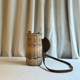 Load image into Gallery viewer, Woven basket with a leather strap on a light surface with curtains in the background
