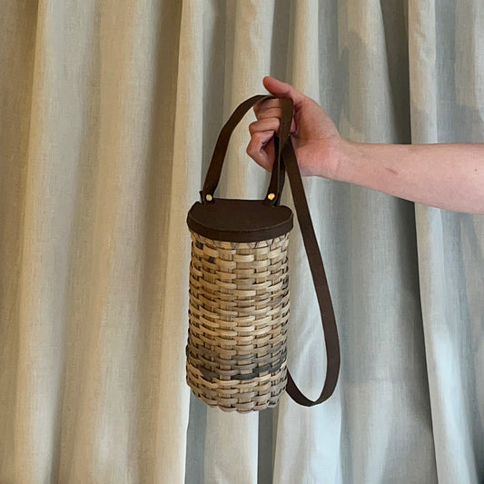Hand holding a woven basket with a leather handle against a curtain background