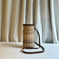 Load image into Gallery viewer, Woven basket with a strap on a white surface with curtains in the background
