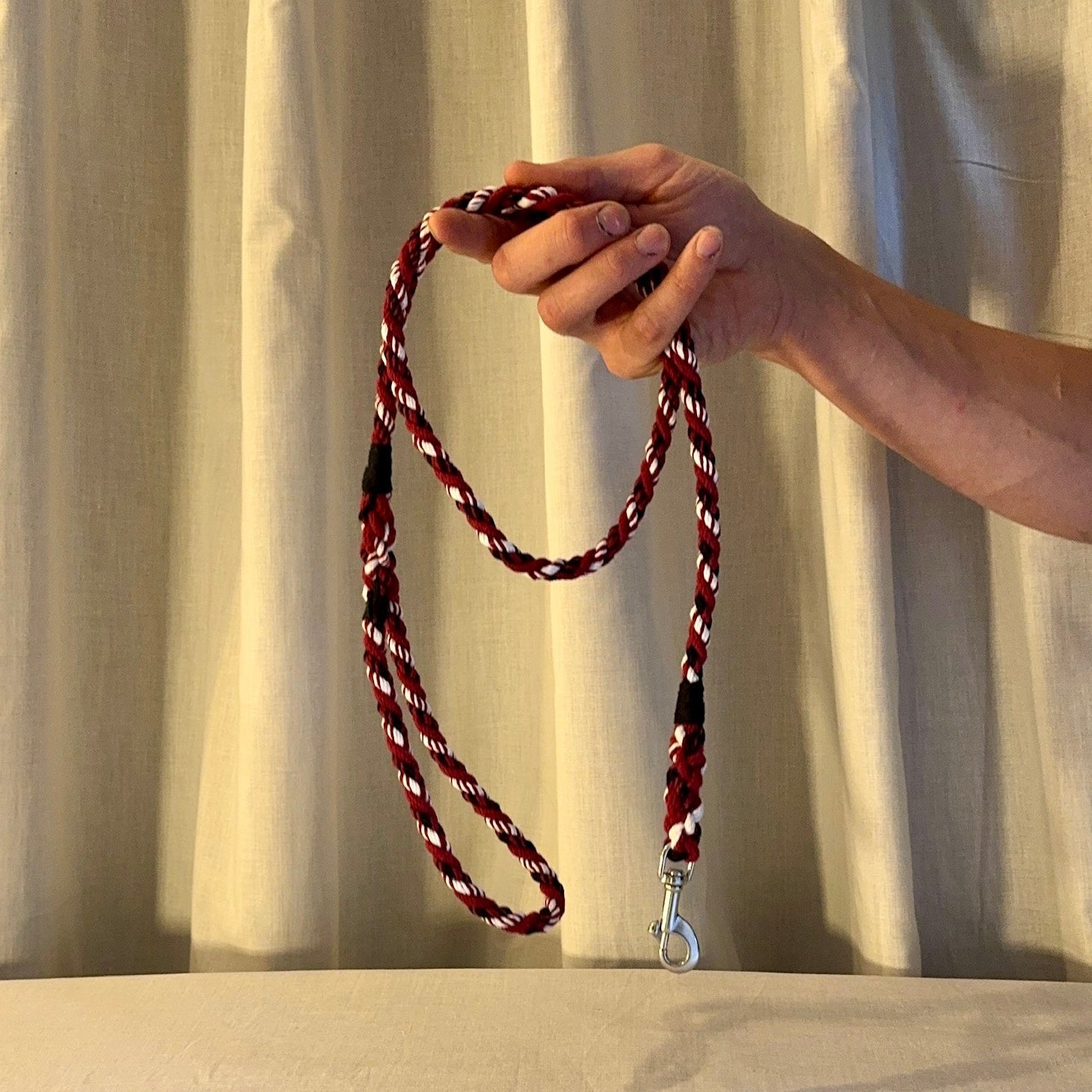 Hand holding a red and white braided lanyard against a plain background