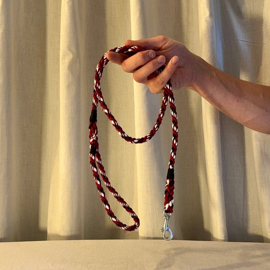 Hand holding a red and white braided lanyard against a plain background