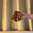 Load image into Gallery viewer, Hand holding two colorful rope juggling  balls against a beige curtain background
