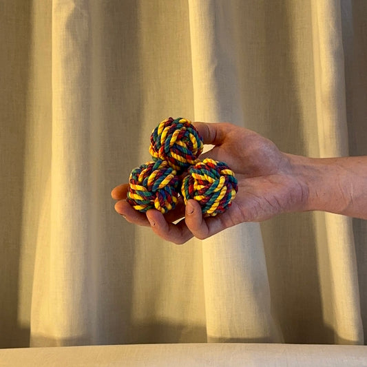 Hand holding two colorful rope juggling  balls against a beige curtain background